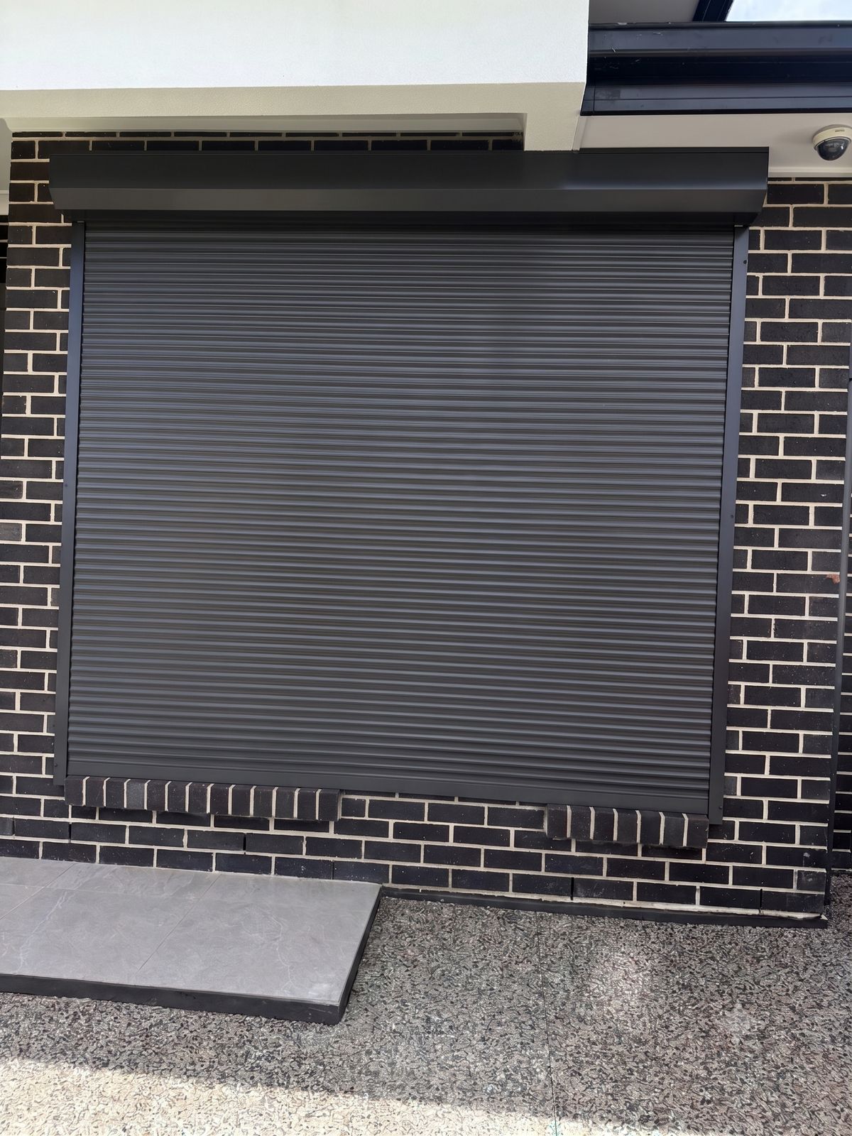 A black roller shutter installed on a brick frontage